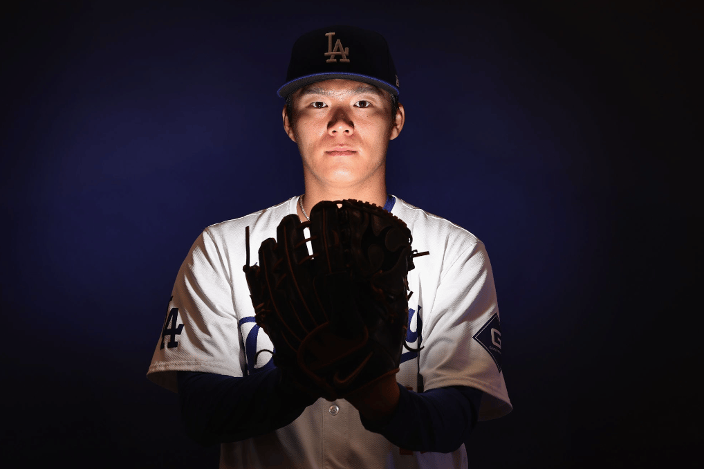 Yamamoto looking at the camera, glove in hand as he pretends to prepare to pitch, with a bright glow coming out of the glove and illuminating his face