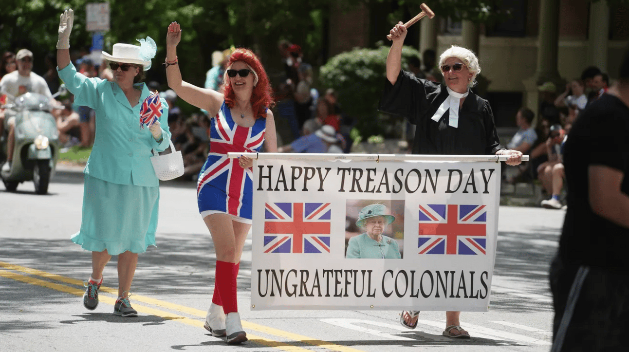 Parade marchers with union jack clothes and a banner with the queen on it saying "Happy Treason Day Ungrateful Colonials"