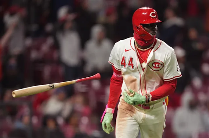 Elly De La Cruz, wearing a red balaclava, his jersey covered in dirt, casually tossing his bat after hitting a homer while looking like a total badass.