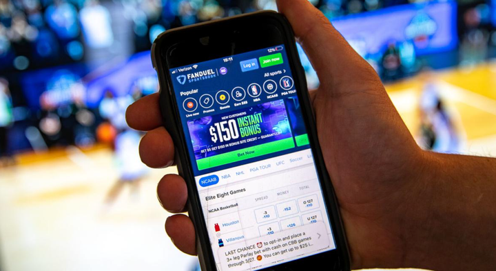 A hand holding a phone with a sports gambling app up